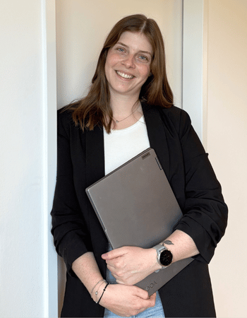 Marketingstrategin Kerstin Rosenthaler lehnt an weißen Türrahmen und hält ihren Laptop in der Hand
